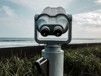 Coin-operated binoculars by sea against sky