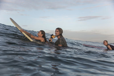 Happy friends with surfboards and camera in ocean