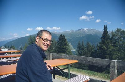 Portrait of man sitting against mountains in sunny day