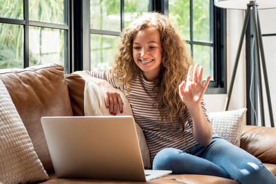 Smiling woman talking on video call while sitting on sofa at home