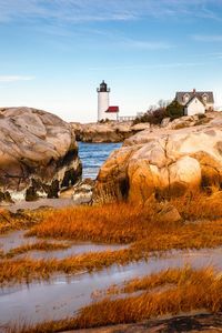 Lighthouse by sea and buildings against sky