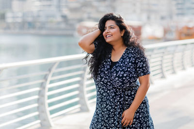 A positive indian girl smiles, strolling along the embankment, straightens her hair.