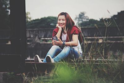 Full length of young woman using mobile phone while sitting outdoors
