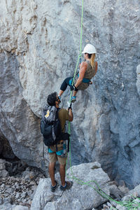 Low angle of active female mountaineer climbing up steep rocky mountain slope while training with male instructor in nature