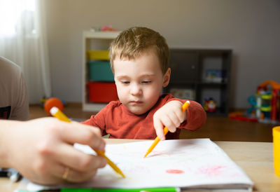 A cute little toddler boy of two years old with dad draws with markers in the album 