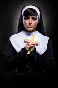 Nun holding cross while standing against black background