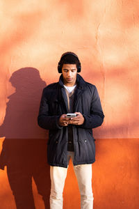 Portrait of young man using phone standing against wall