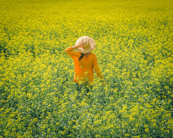 Rear view of woman standing amidst yellow flowering plants on field