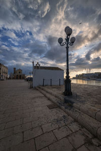 Street light on footpath by buildings against sky