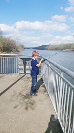 Boy standing on railing against sky