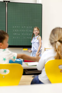 Smiling girl standing against blackboard in classroom at school