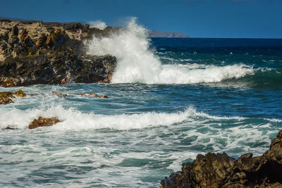 Waves splashing on rocks against sky