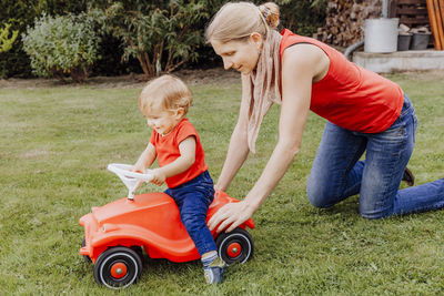 Mother pushing son sitting on toy car in yard