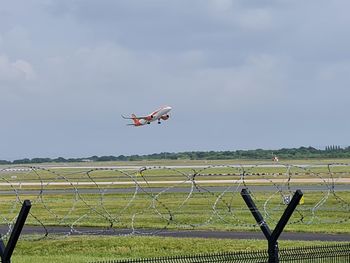 Airplane flying over field against sky