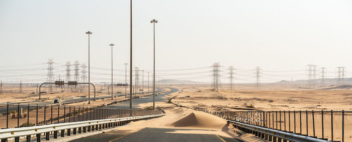 Road by electricity pylon against clear sky