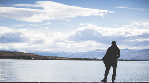 Rear view of man standing by lake against sky