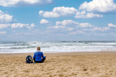 Woman sitting on the beach practicing meditation observing the horizon of the sea. 
