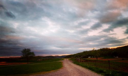 Road amidst field against dramatic sky