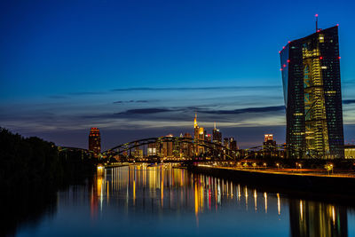 Illuminated buildings reflecting on river in city at dusk