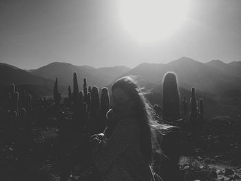 Young woman standing by cactus on mountains against sky