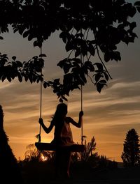 Silhouette woman swinging against sky during sunset