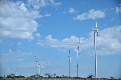 Low angle view of wind turbines on field against sky