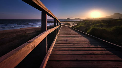 View of wooden bridge over sea at sunset