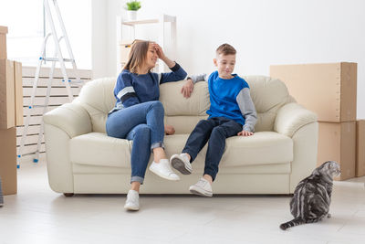 Full length of friends sitting on sofa at home