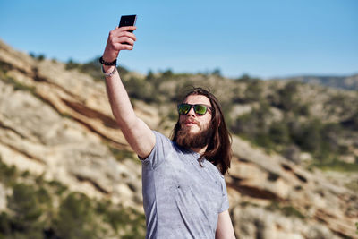 Young man wearing sunglasses talking selfie while standing on mountain
