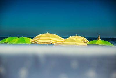 Close-up of multi colored umbrellas on beach against clear blue sky