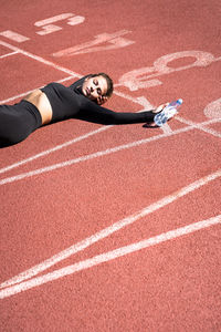 High angle view of tired woman lying with water bottle on running track