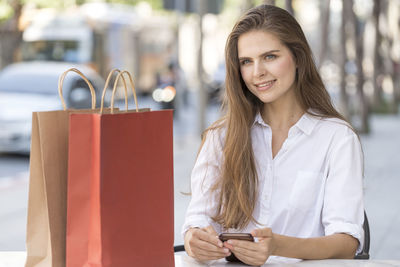 Portrait of young woman with shopping bags sitting outdoors