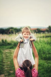 Woman with baby raised on field against sky