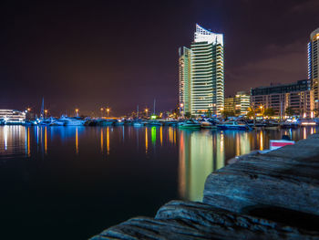 Illuminated buildings by sea against sky at night