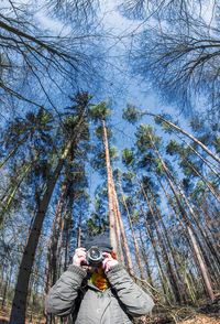 Low angle view of man photographing while standing against trees in forest