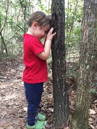 Side view of boy standing by tree trunk in forest