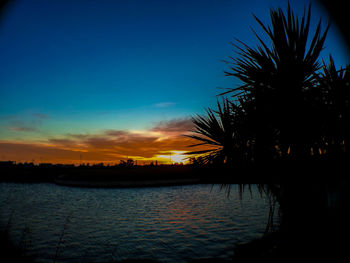 Silhouette trees by lake against sky at sunset