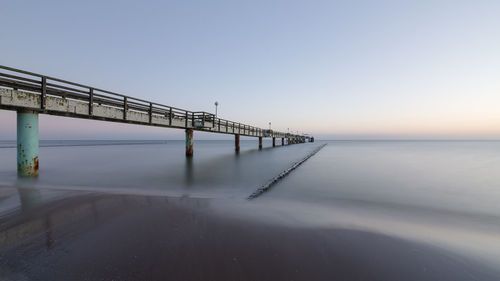 Pier over sea against clear sky during sunset