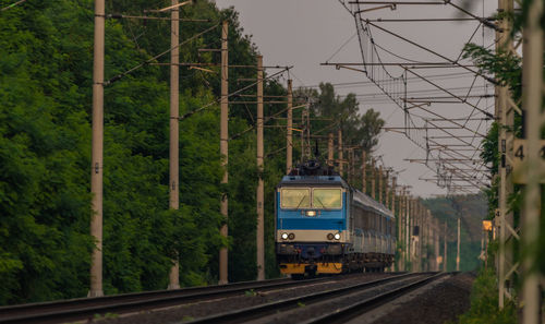 Train on railroad track by trees against sky