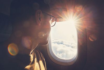 Man looking through airplane window during sunny day