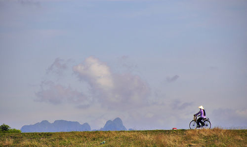 Woman riding bicycle on field against sky