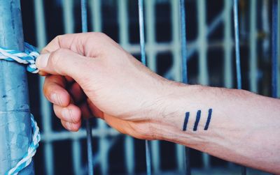 Cropped hand of man holding rope tied on metal pole