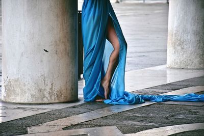 Low section of woman in blue gown standing by column