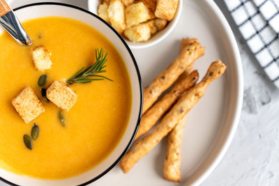 Top view of pumpkin, carrot cream soup in a bowl. with croutons, pumpkin seeds and bread sticks