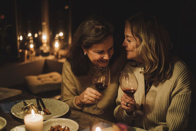 Senior female friends talking and holding wineglasses during candlelight dinner party