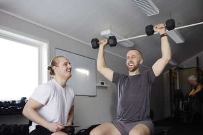 Man exercising with dumbbell with trainer checking his progress