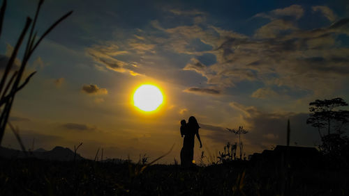 Silhouette woman and his child standing on field against sky during sunset