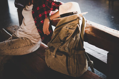 Midsection of woman with backpack and hat sitting on bench 