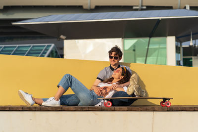 Stylish man and woman enjoy sunset cuddling at longboard relaxing after skateboarding in skate park