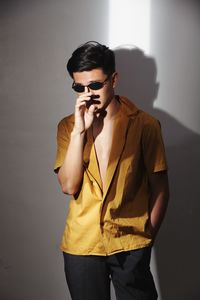 Young man wearing sunglasses standing against wall